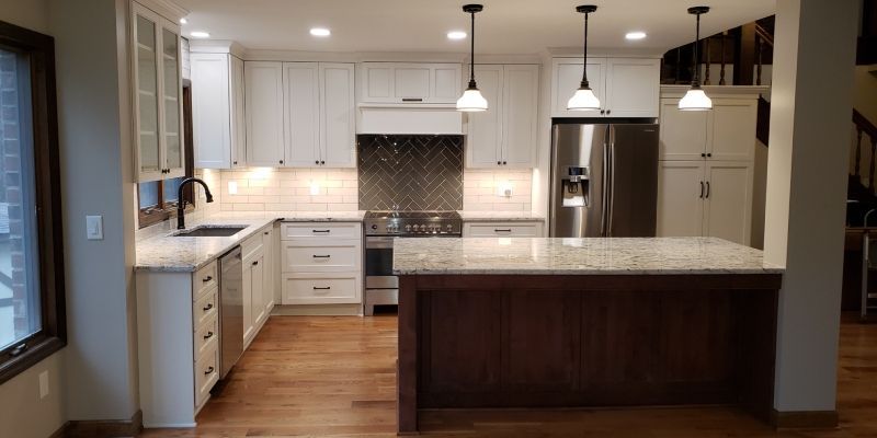 Modern kitchen with white cabinets, dark island, pendant lights, and wood floors