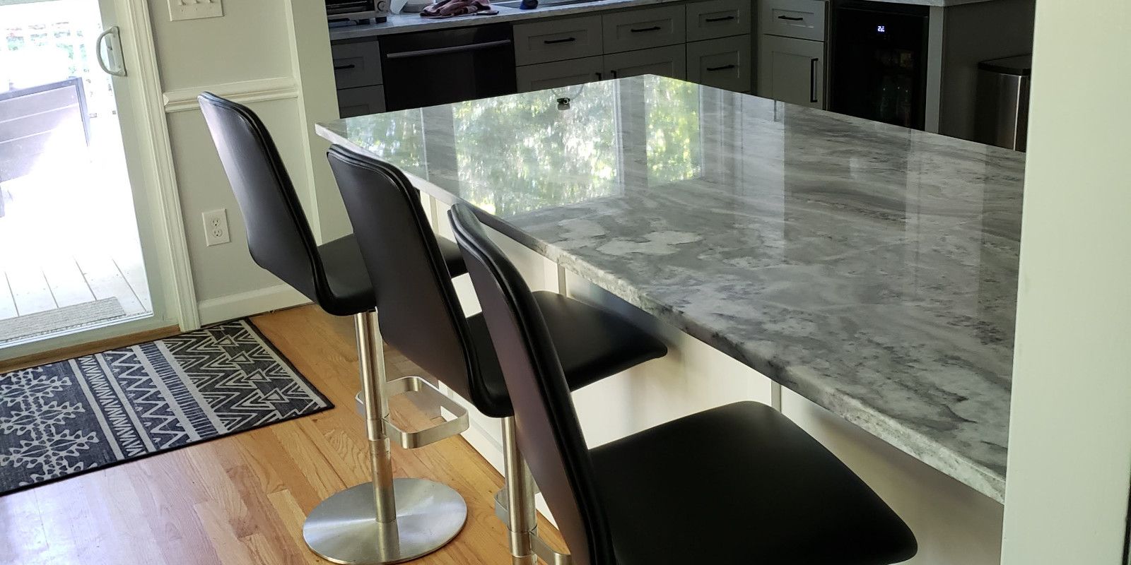 Kitchen island with two black bar stools beside a marble countertop and a windowed door.