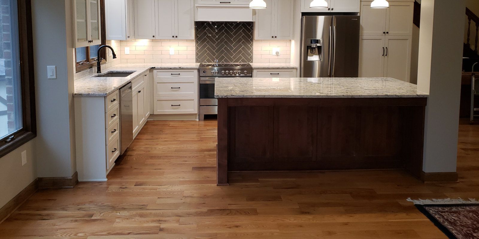 Spacious modern kitchen with white cabinets, granite island, and warm wood flooring