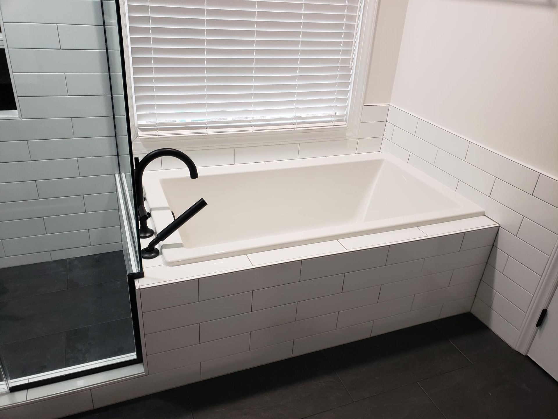 Modern white bathroom with a built-in bathtub, black faucet, tiled walls, and a window above the tub