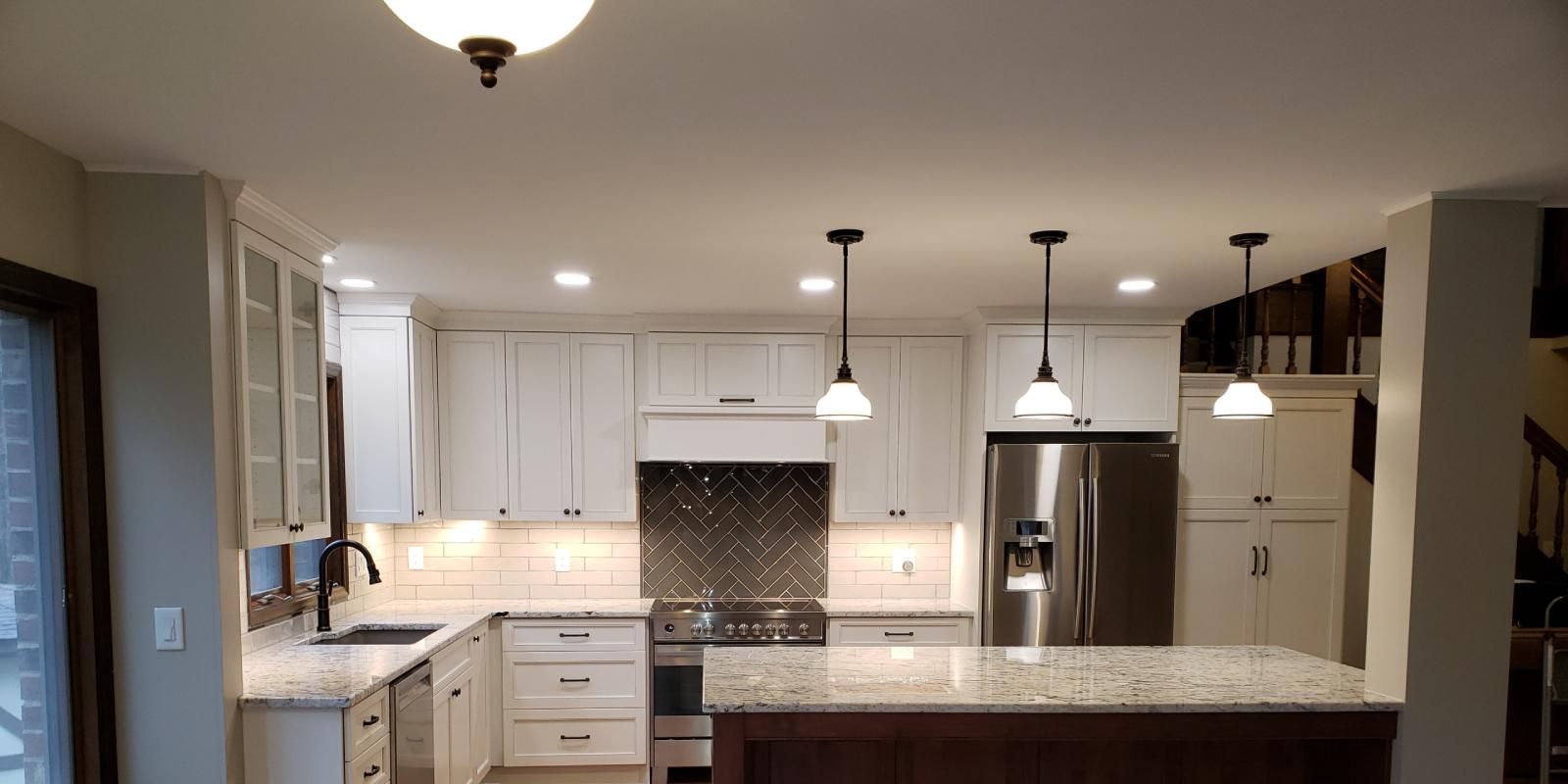 Bright modern kitchen with white cabinets, granite island, pendant lights, and stainless steel appliances