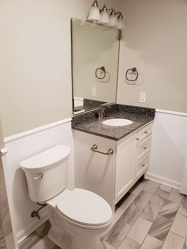 Small bathroom with toilet, vanity sink, mirror, and gray patterned tile floor.