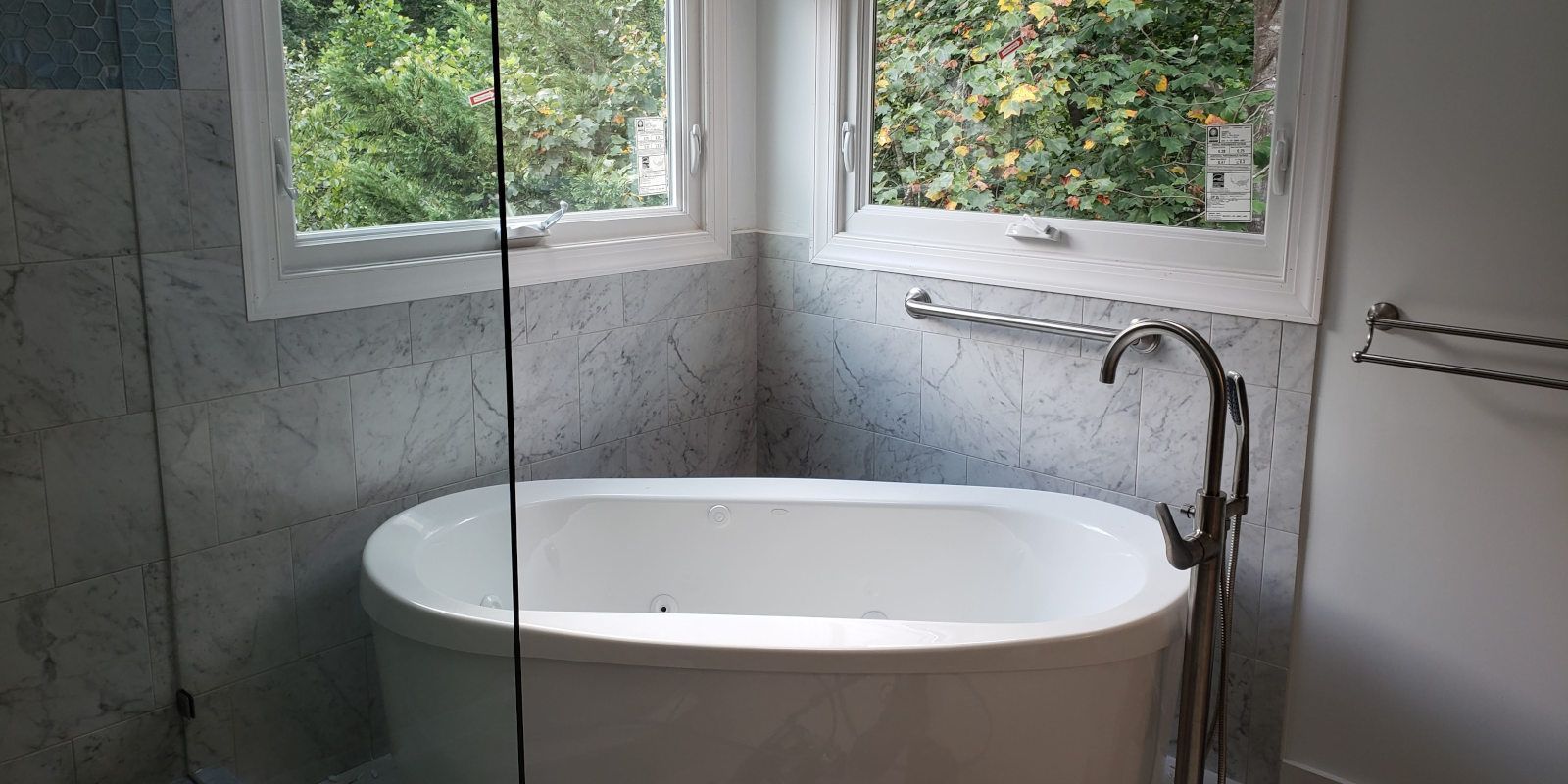 Modern bathroom with a white freestanding tub beside a window and wall-mounted faucet