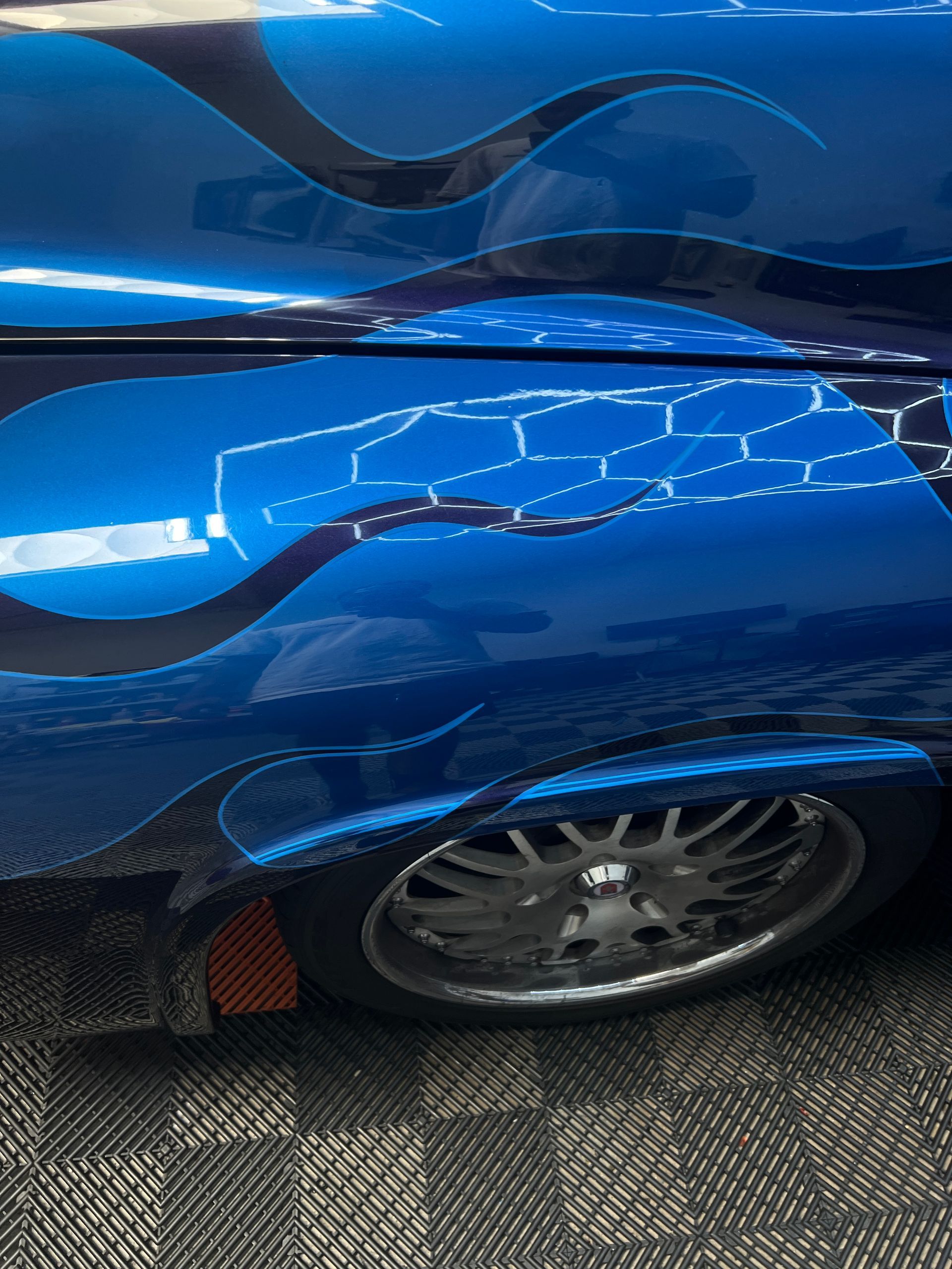 A blue car with flames painted on the side is parked on a carpeted floor.