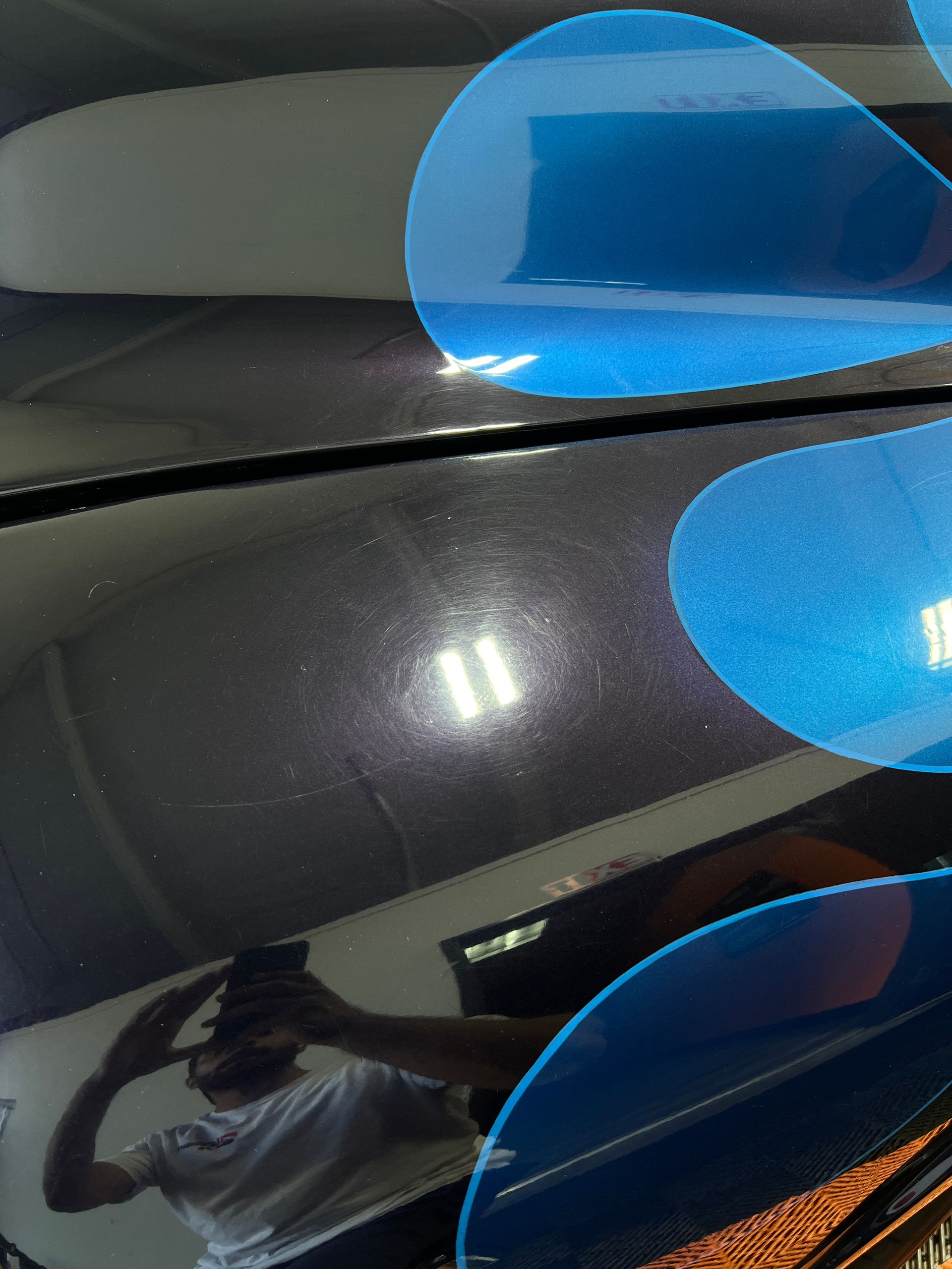 A man is taking a picture of a black car with blue circles on it.