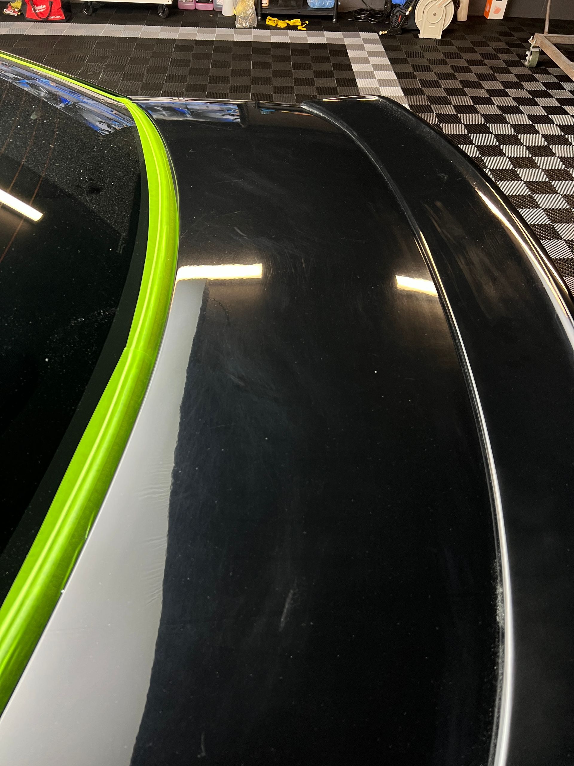 A black car with a green stripe on the hood is parked in a garage.