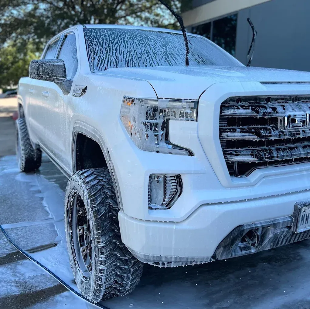White pickup truck covered in soap suds, being washed outdoors in a driveway
