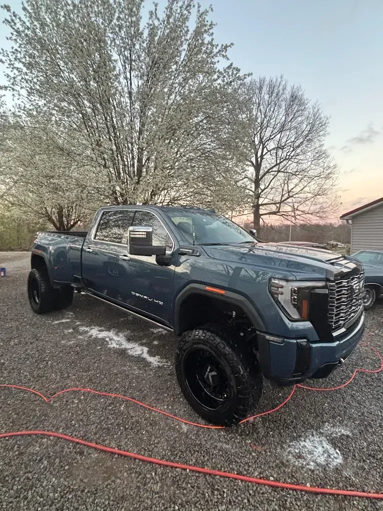 Dark gray pickup truck parked on a gravel drive beside trees at dusk
