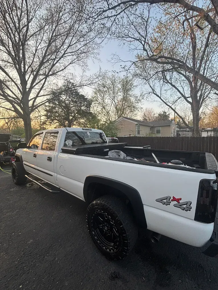 White lifted pickup truck parked on a street at dusk, viewed from the rear side.