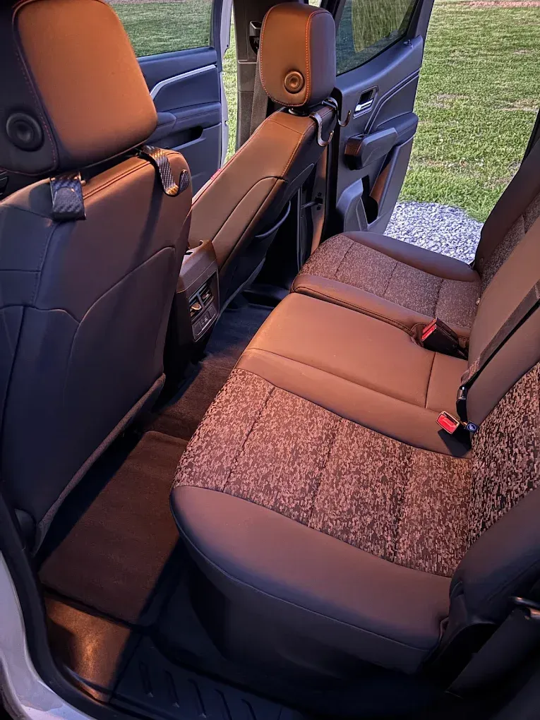 Open car rear seat with brown-and-gray fabric upholstery and the door open to a grassy outdoor area