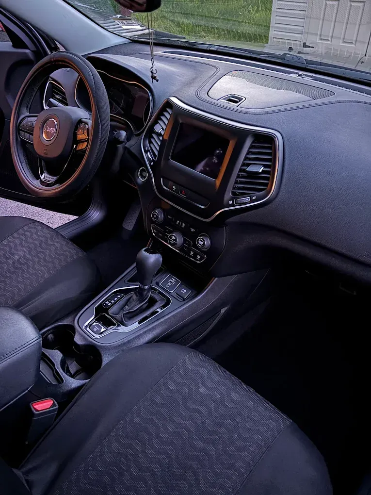 Car interior with black seats, steering wheel, dashboard, center console, and gear shifter.