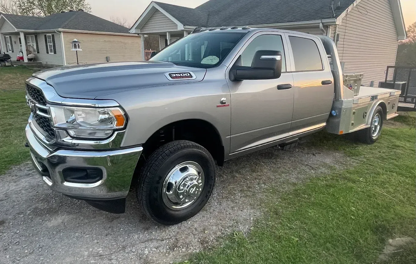 Silver heavy-duty pickup truck parked in a driveway with a flatbed trailer behind it