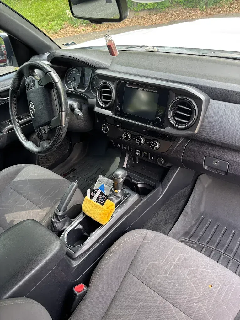 Car interior with black dashboard, center console, and gray seats, with a small organizer and tools in the cup holder area