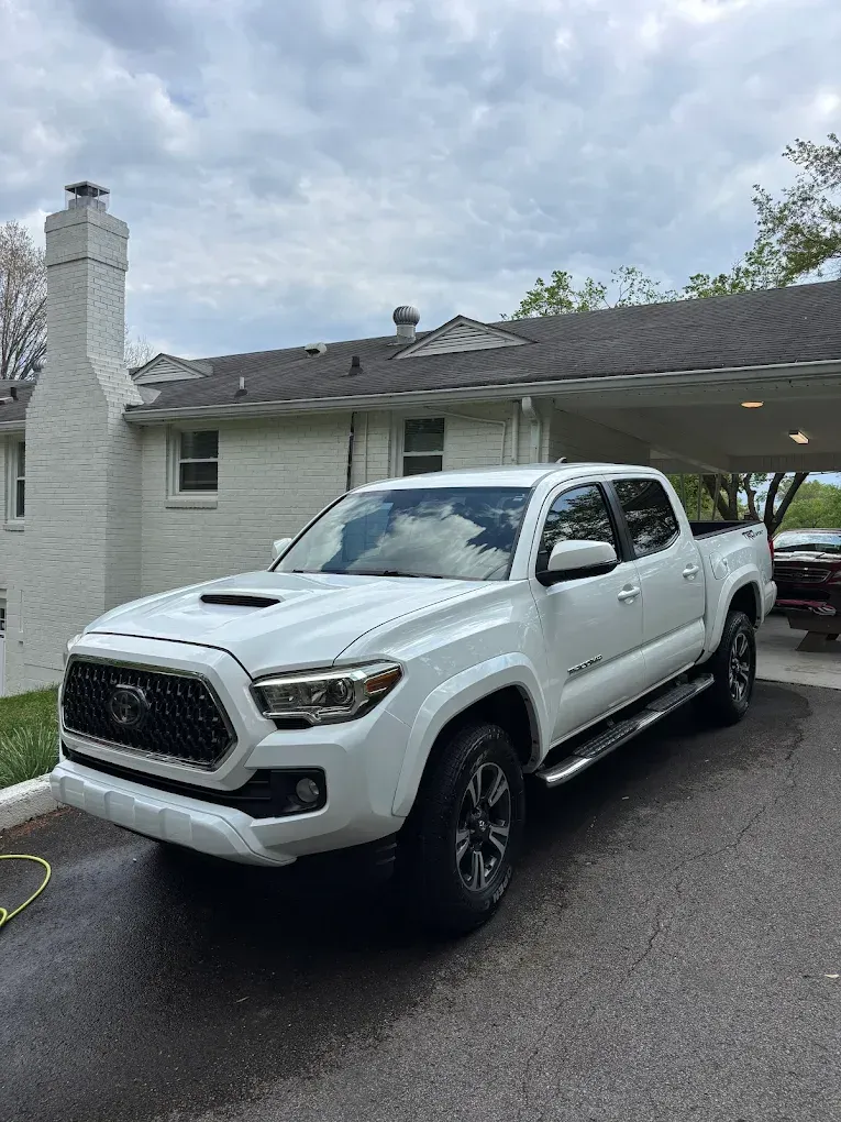 White pickup truck parked in a driveway beside a house under cloudy skies