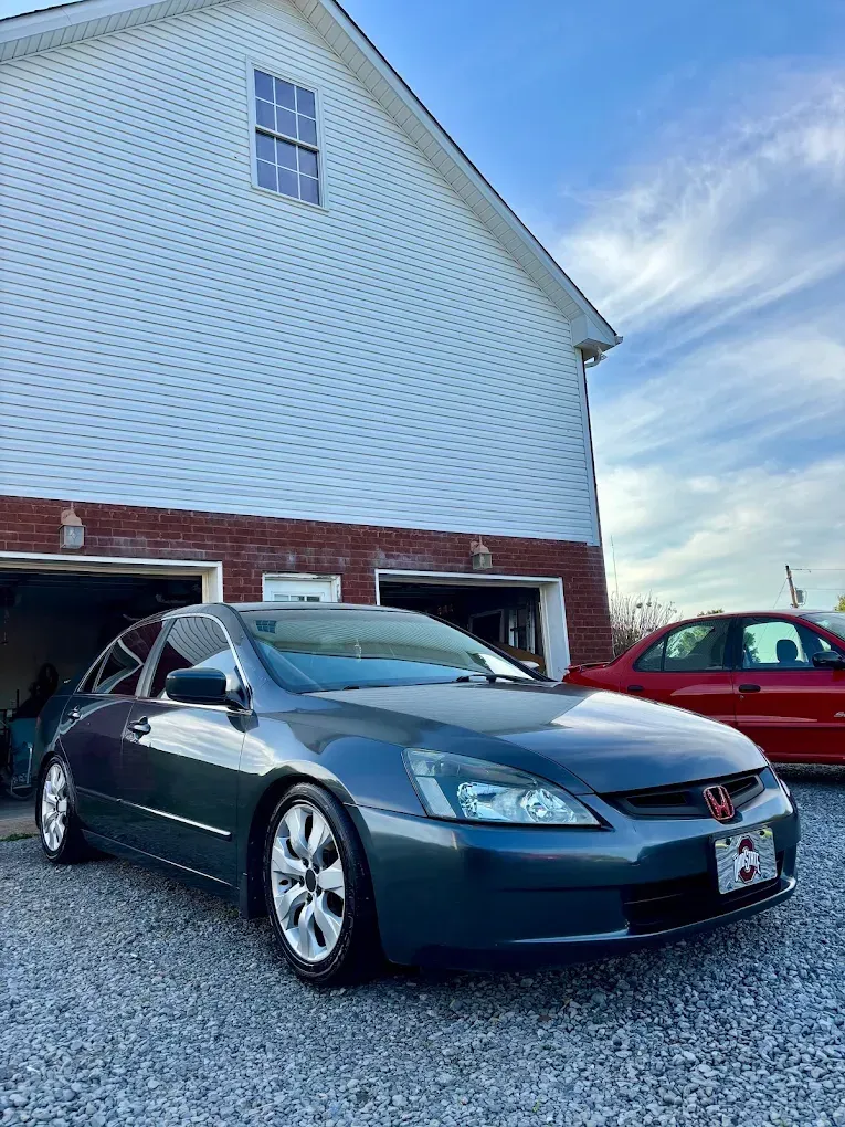 Dark gray sedan parked in front of a white house with a red brick base on a driveway