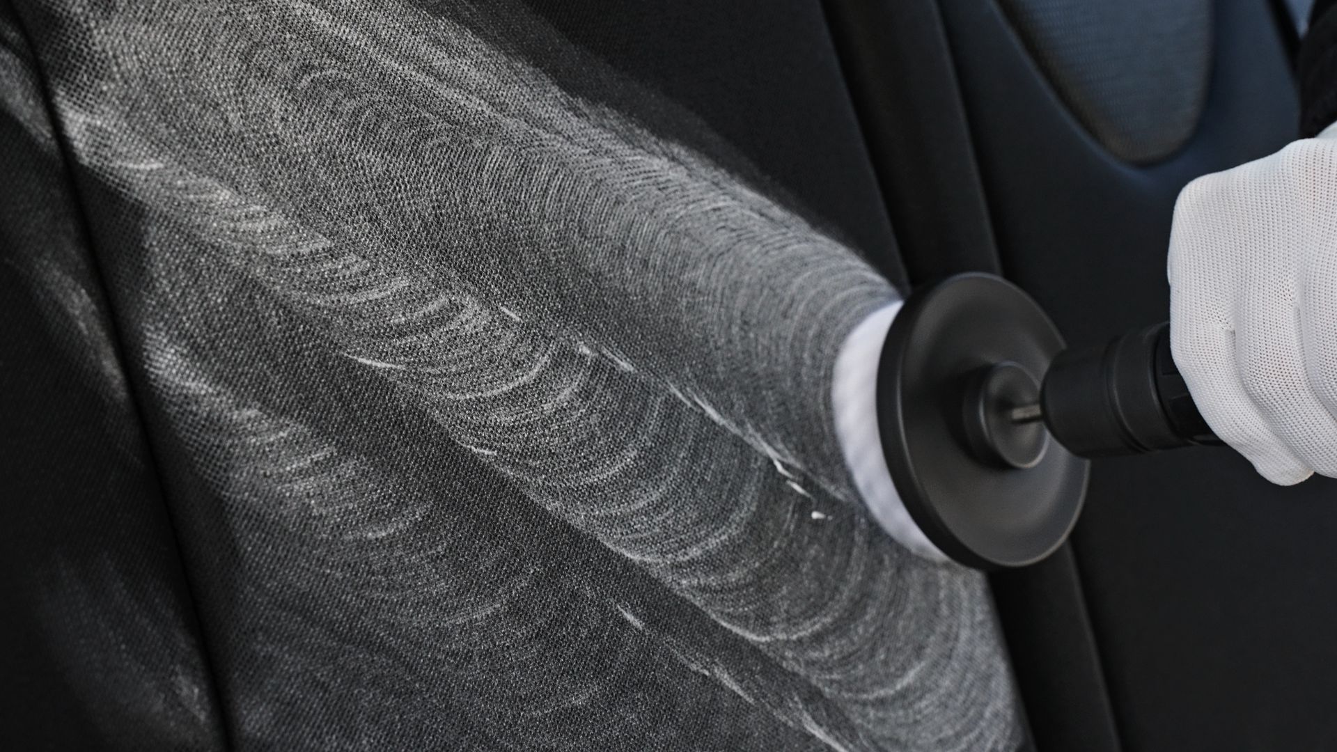 Handheld vacuum cleaning dust from a black car seat fabric
