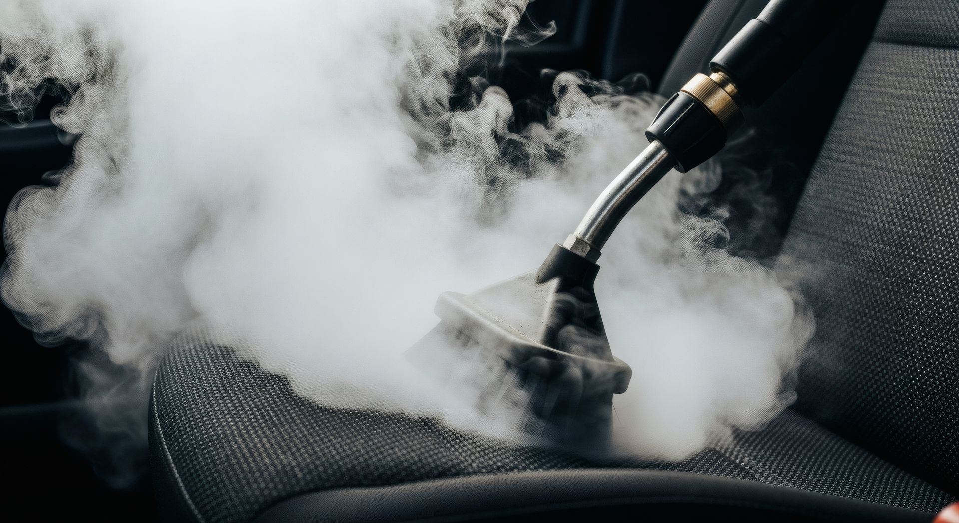 Steam cleaning a black car seat with a handheld extractor nozzle