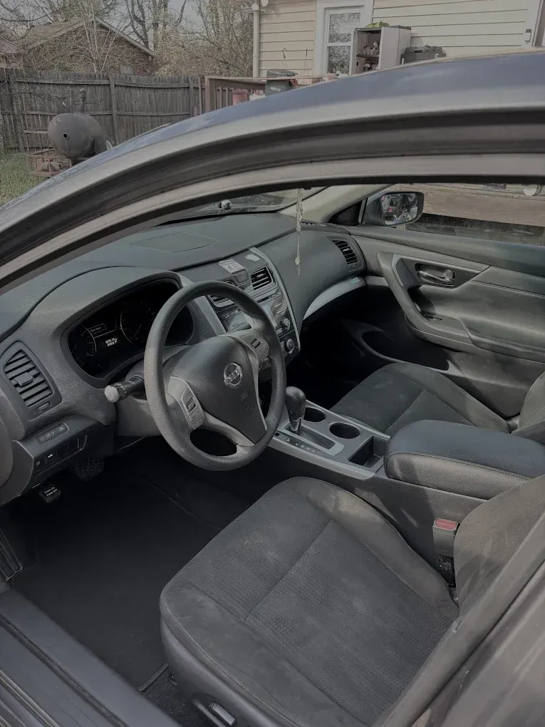Interior of a gray Toyota sedan, showing the front seats, steering wheel, and dashboard from the open driver’s side.