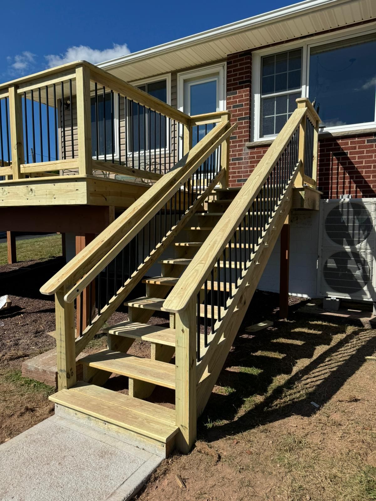 A wooden deck with stairs leading up to it and a brick house in the background.