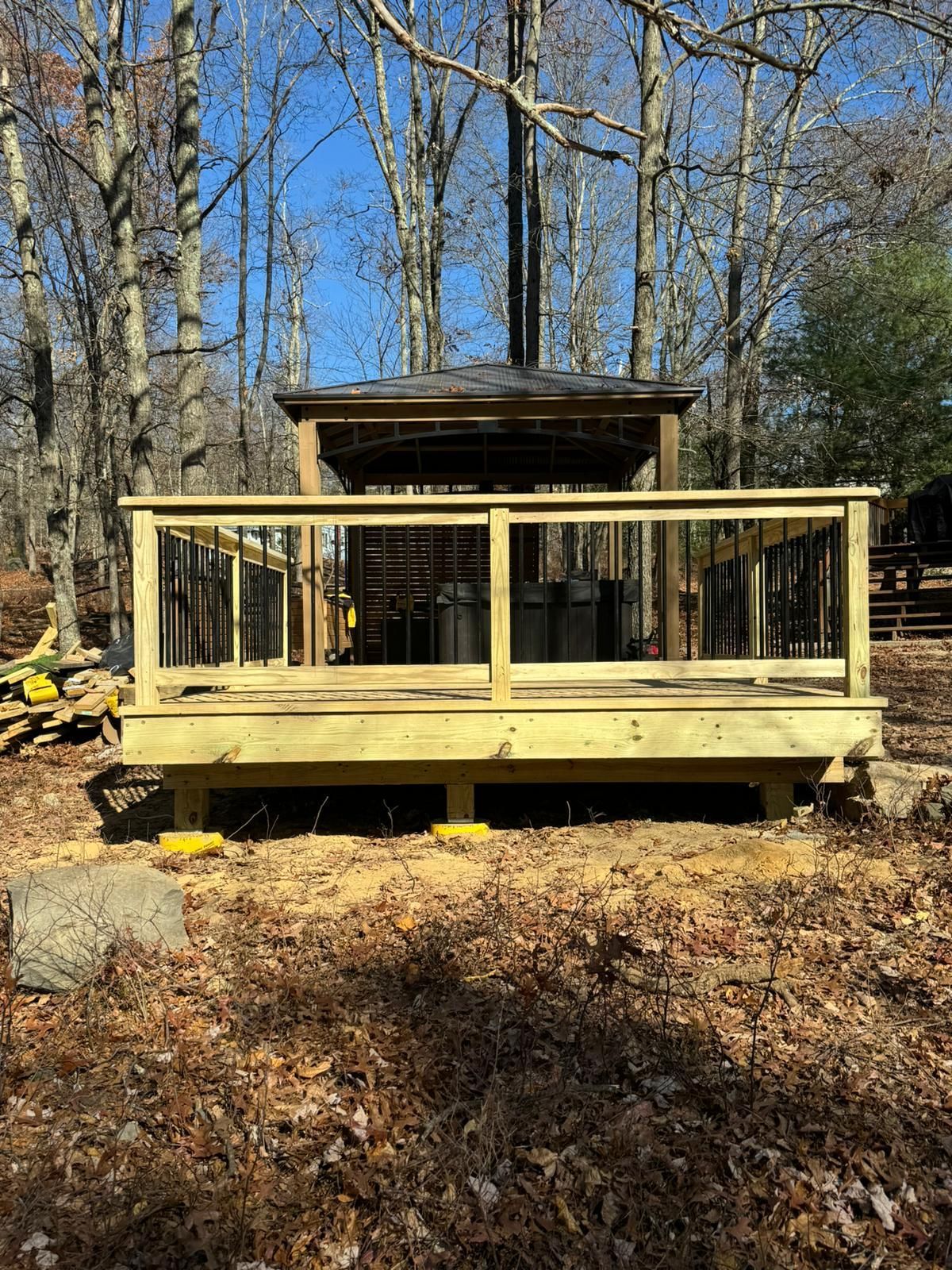 A wooden deck is being built in the woods next to a gazebo.