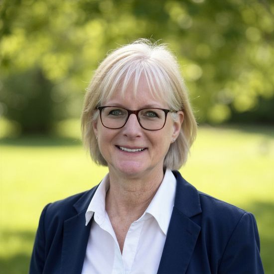 A woman is sitting at a desk with a laptop and a vase of flowers.