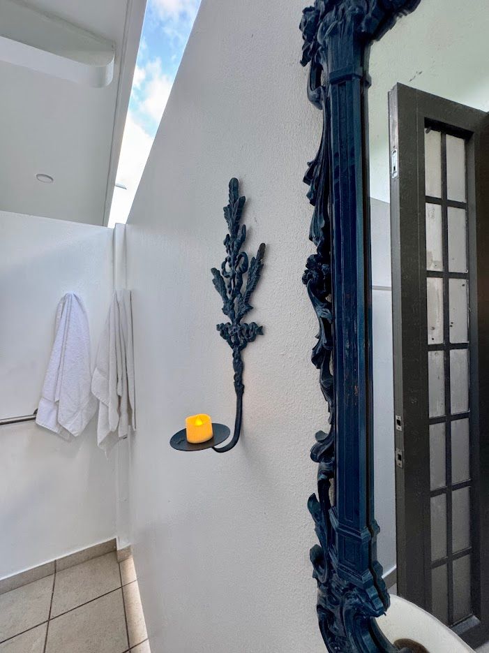 A blue wall sconce with a candle, next to an ornate blue mirror and a door in a white room.