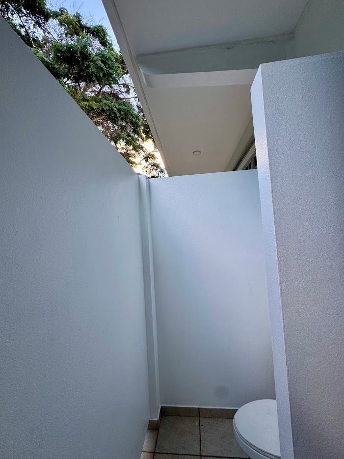White-walled outdoor space with a table and glimpse of sky and trees above.