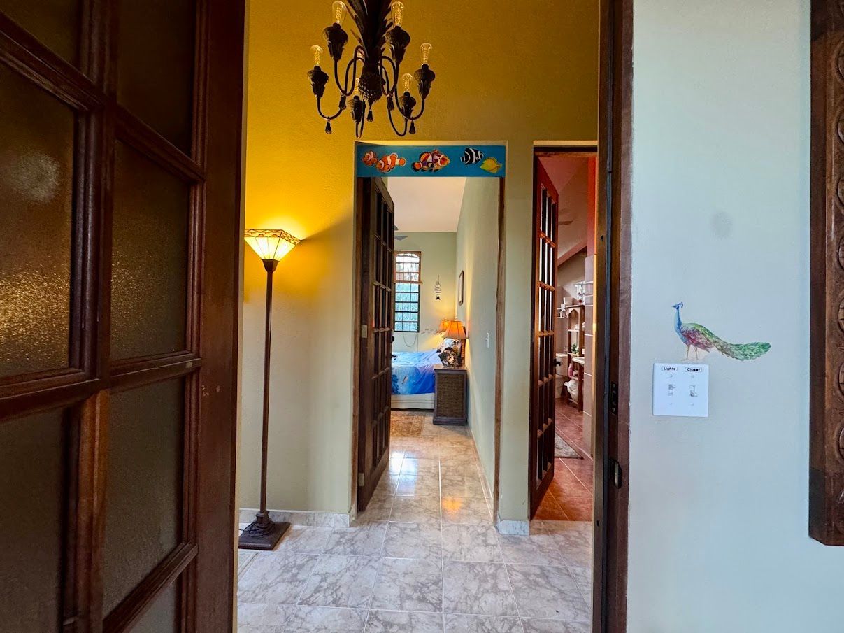 Hallway with open doors, featuring a chandelier, a floor lamp, and a peacock sticker on the wall.