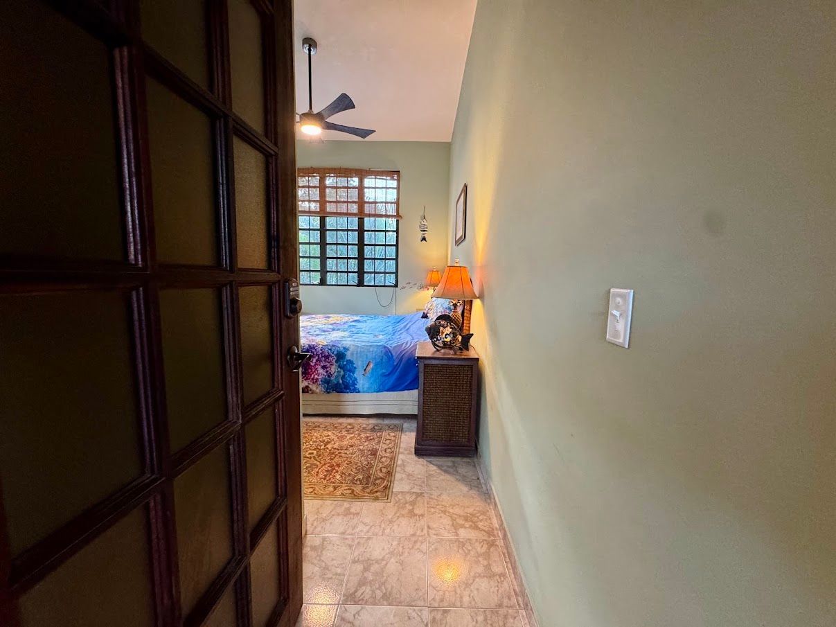 Open doorway reveals a bedroom with bed, nightstand, and window. Green wall and tiled floor.