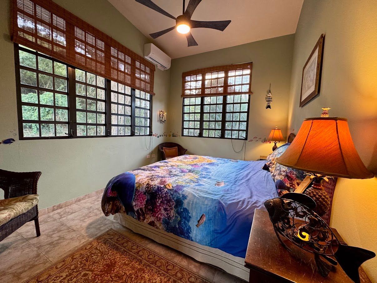 Bedroom with bed, windows, and lamp; green walls, floral bedspread.