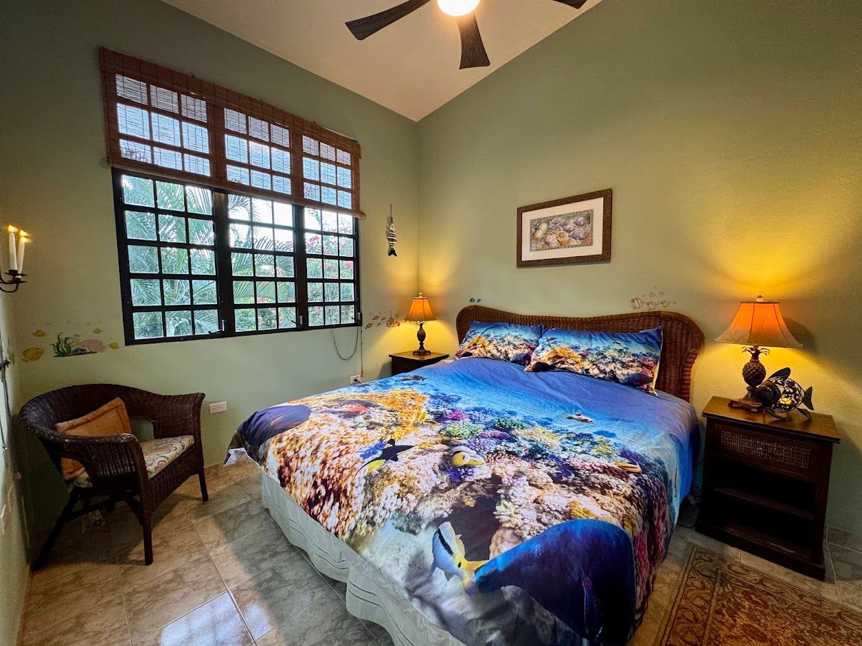 Bedroom with bed, wicker furniture, green walls, large window, and underwater-themed bedding.
