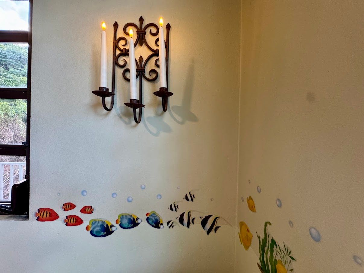 Wall with decorative fish decals, candle sconce, and window to a view of foliage.
