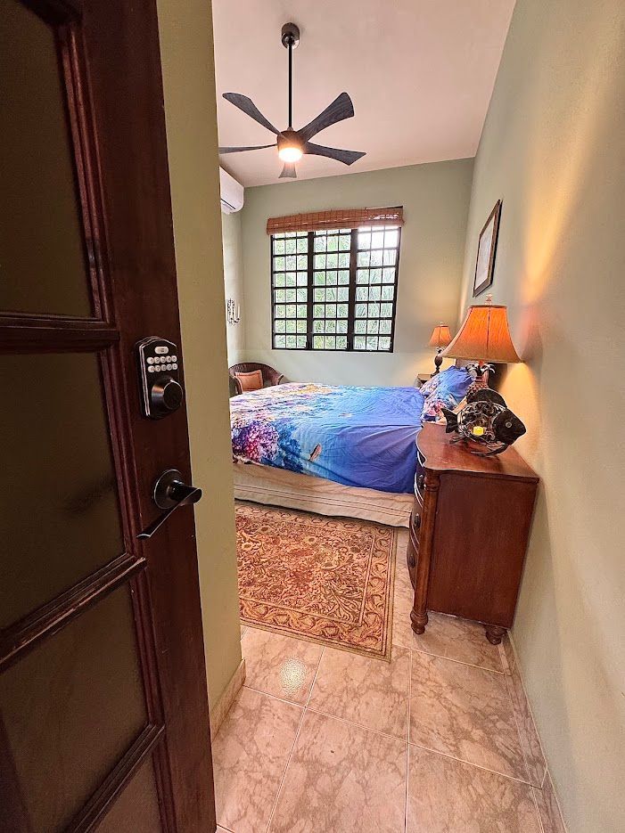 Bedroom interior. Bed with blue floral comforter, wooden nightstand, open doorway.