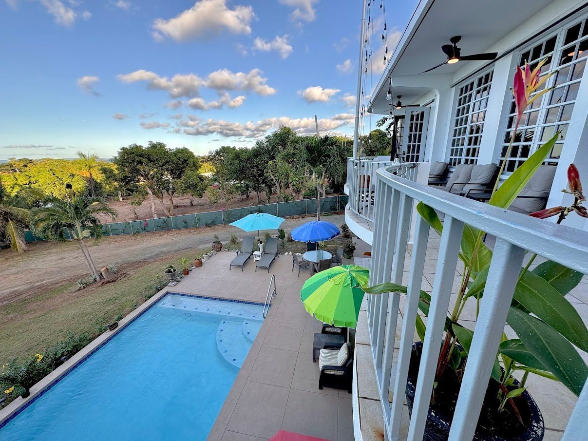 Poolside view with pool, umbrellas, and building with balcony, blue sky.