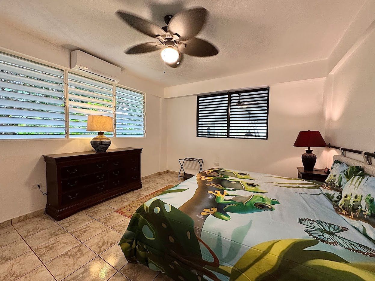 Bedroom interior with bed, dresser, lamps, window with blinds, and ceiling fan.