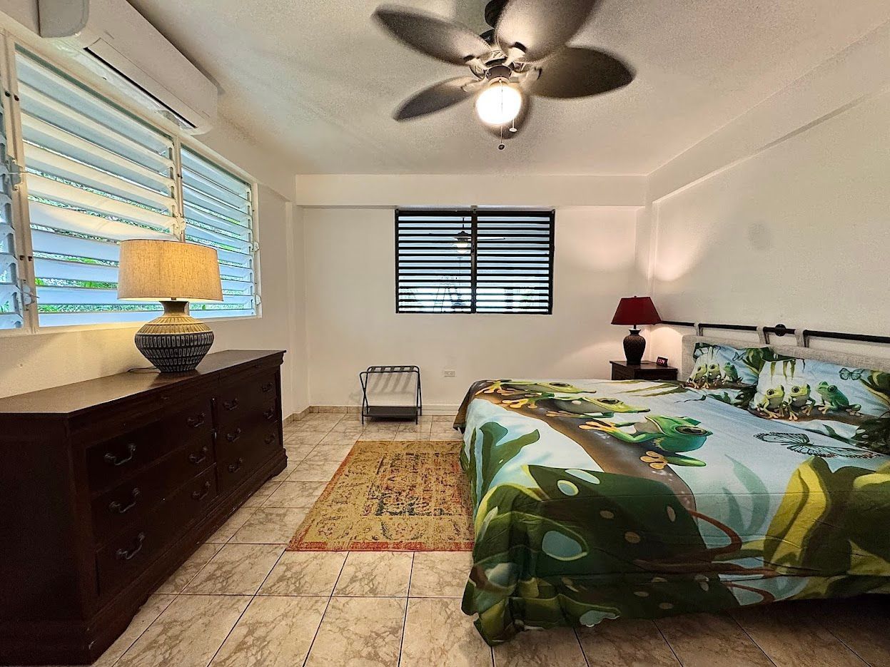 Bedroom with a bed, dresser, windows, rug, and ceiling fan.