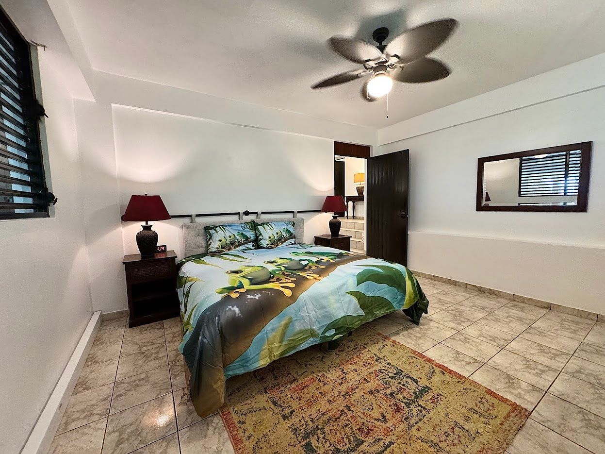 Bedroom with a bed, nightstands, rug, and ceiling fan. Features light walls, a window, and a dark door.