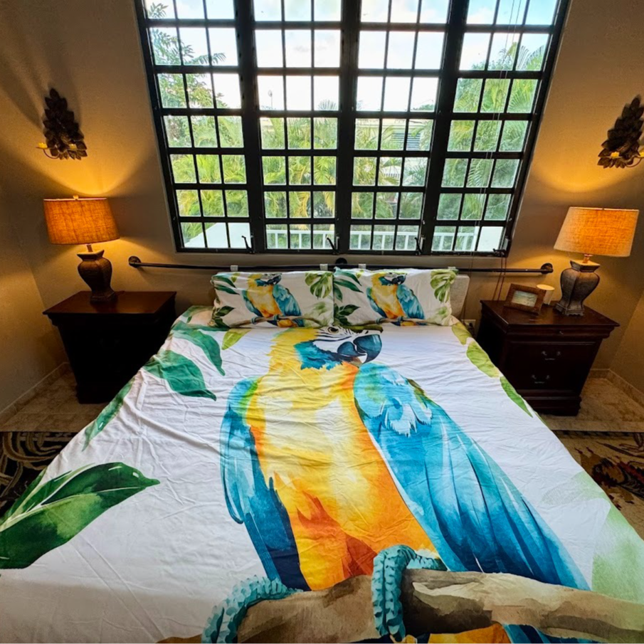 Bedroom with parrot-themed bedding, dark wood furniture, and large window overlooking trees.