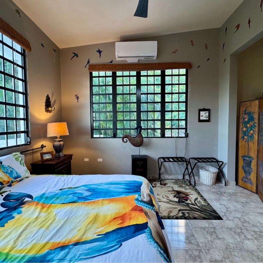 Bedroom with a bed, large windows, and bird wall decor. The bed has a colorful, patterned bedspread.