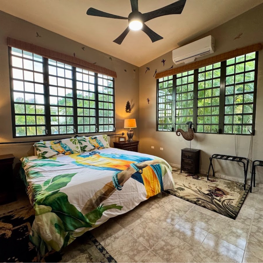 Bedroom with large windows, colorful bedding, and ceiling fan.
