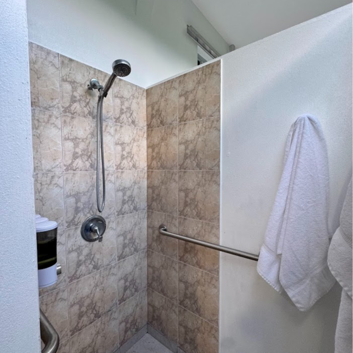 Shower stall with marble-look tile and grab bar, white towel hangs.