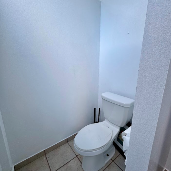 Toilet in a small bathroom with light blue walls and beige tile floor.