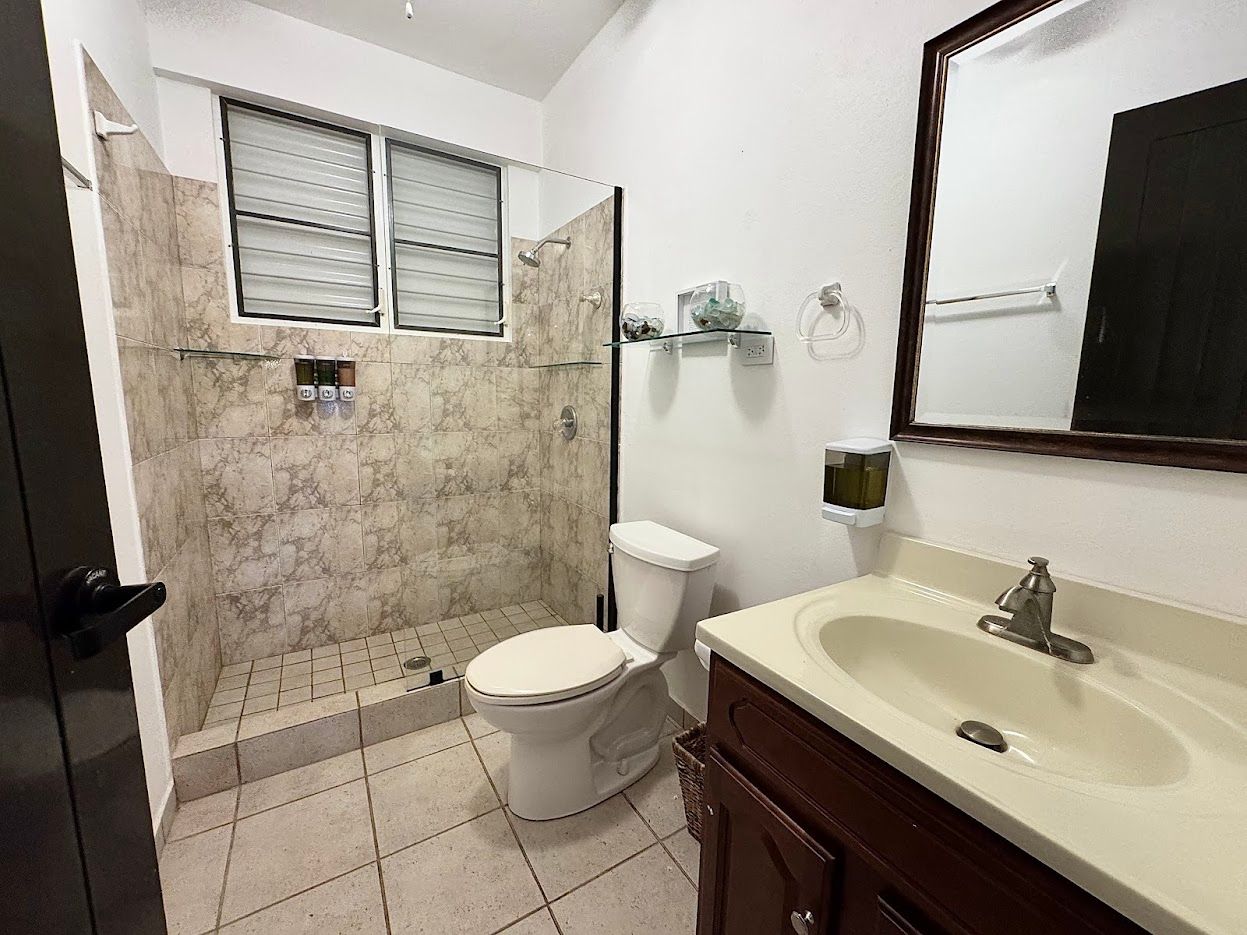 Bathroom with a shower, toilet, and sink. Beige tile and dark wood vanity.