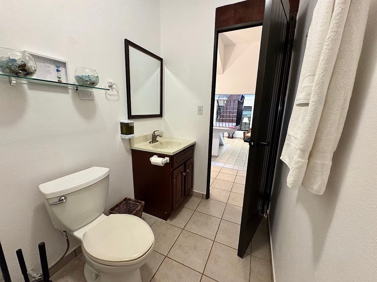 Small bathroom with a toilet, sink, mirror, and open doorway to another room. A towel hangs on the door.