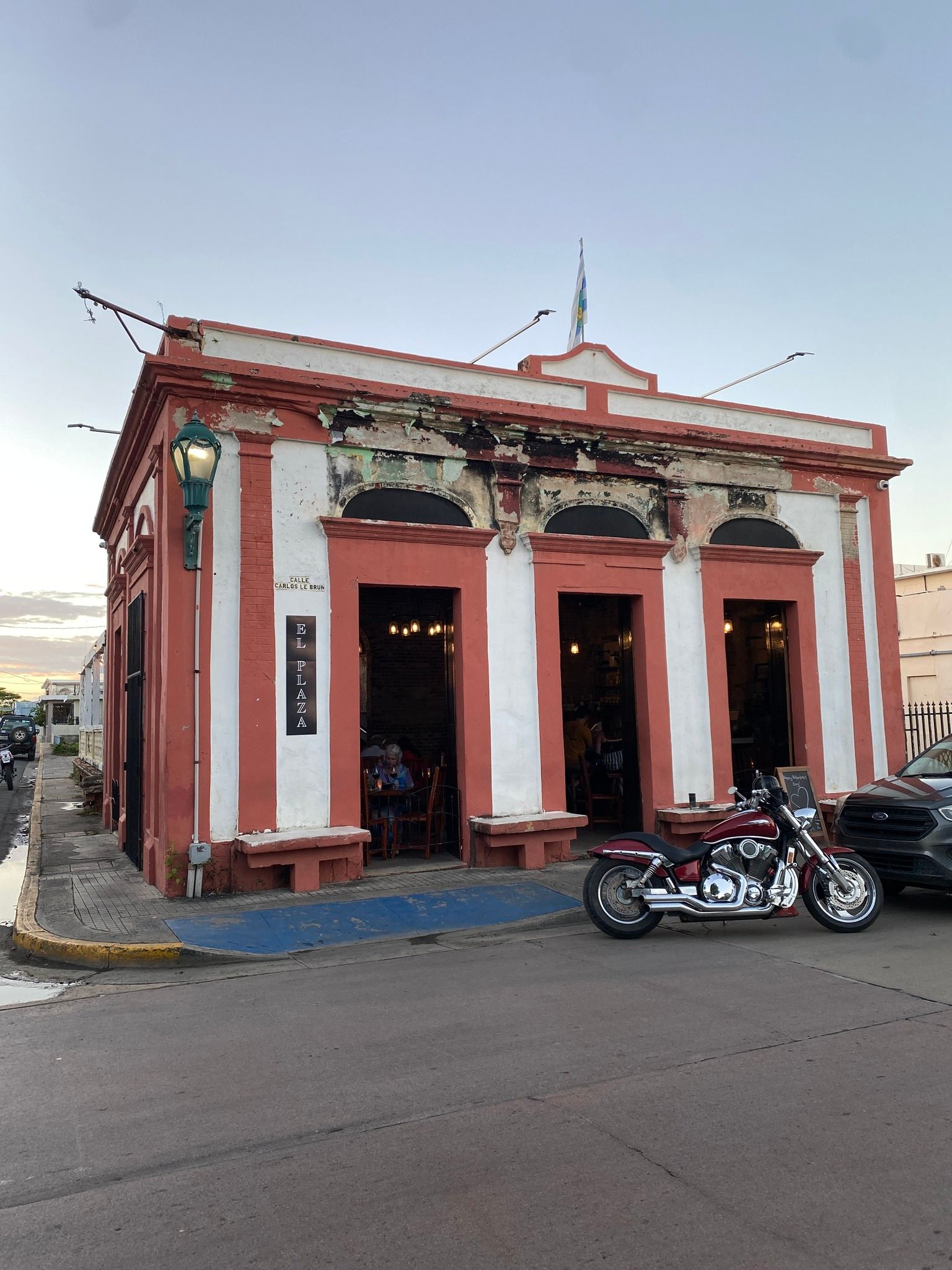 Outdoor restaurant with people seated at tables, palm trees, cocktails, blue sky.