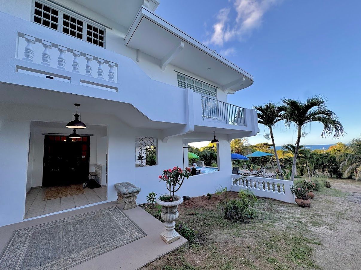 White two-story house with balcony, entryway, and ocean view on a sunny day.