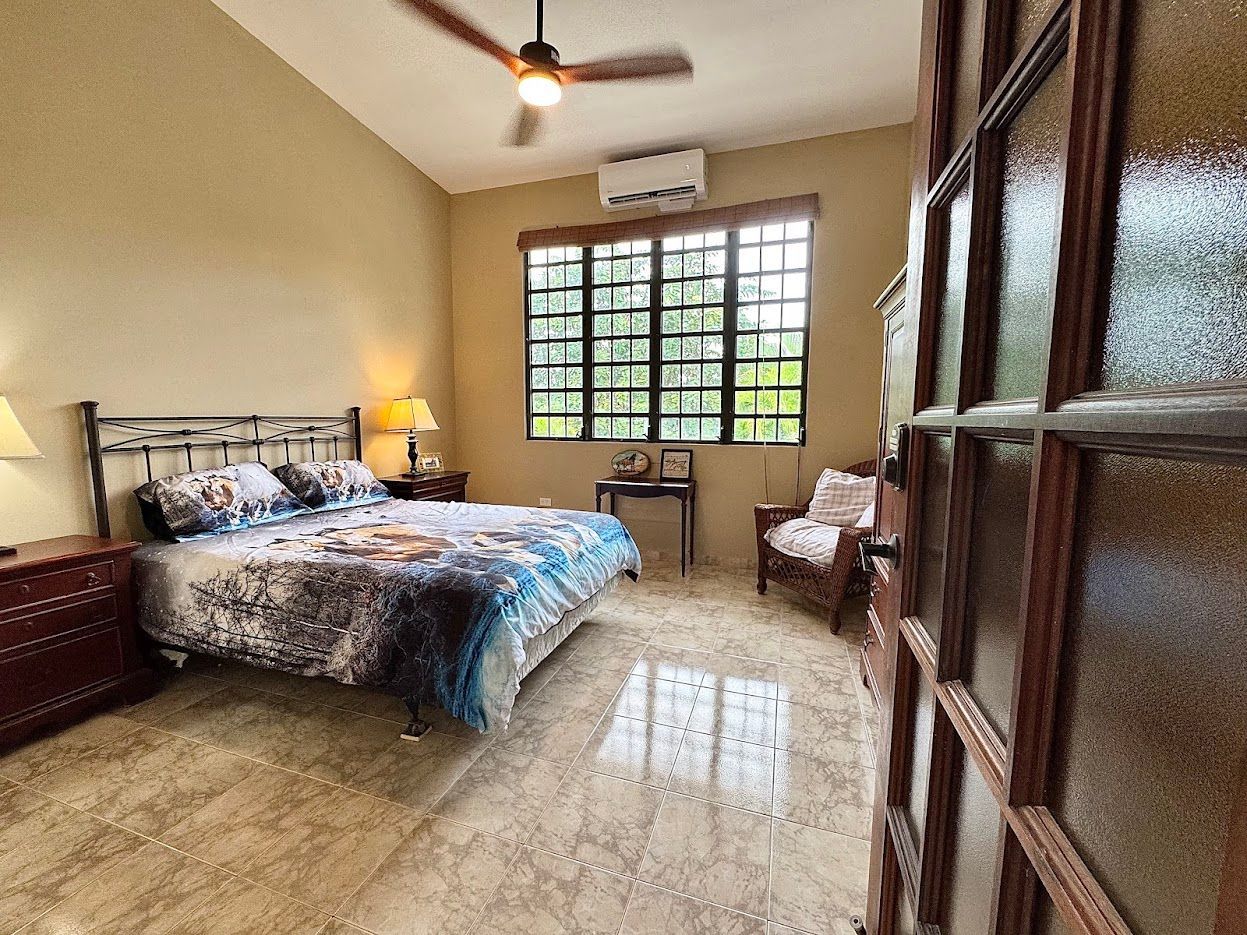 Bedroom with a bed, a window, and a ceiling fan; light beige walls and glossy floor.
