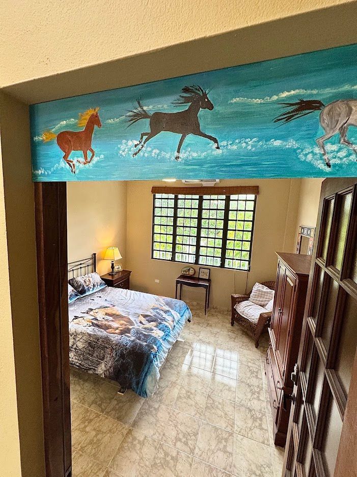 Bedroom interior with painted horses above the doorway. Bed, window, and furniture visible.