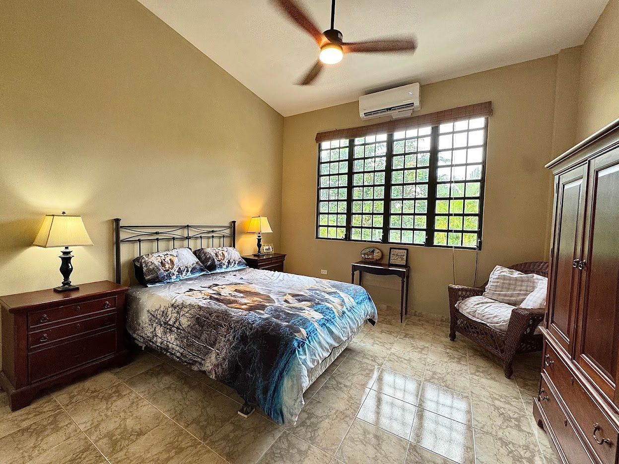 Bedroom with bed, nightstands, chair, wardrobe, and window with outdoor view. Brown and beige tones.