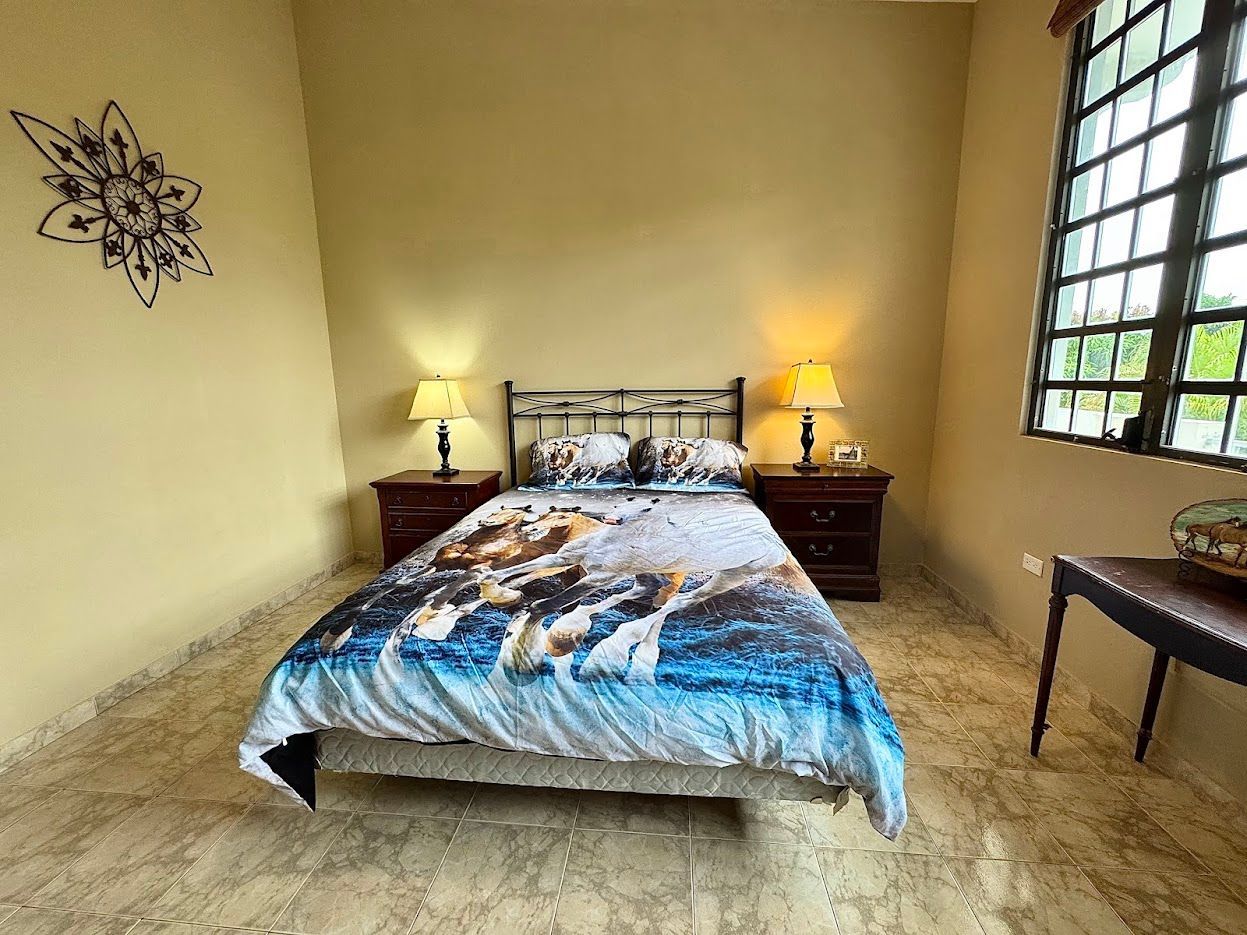 Bedroom with a bed, two nightstands, a window, and wall decor. The bed has a blue and white comforter.